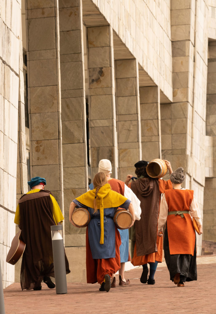 Os actores do espectáculo Arte sen guión, de Galeateatro, vestidos con roupas medievais e cargando con barricas de viño, camiñando de espaldas pola Cidade da Cultura, en Santiago